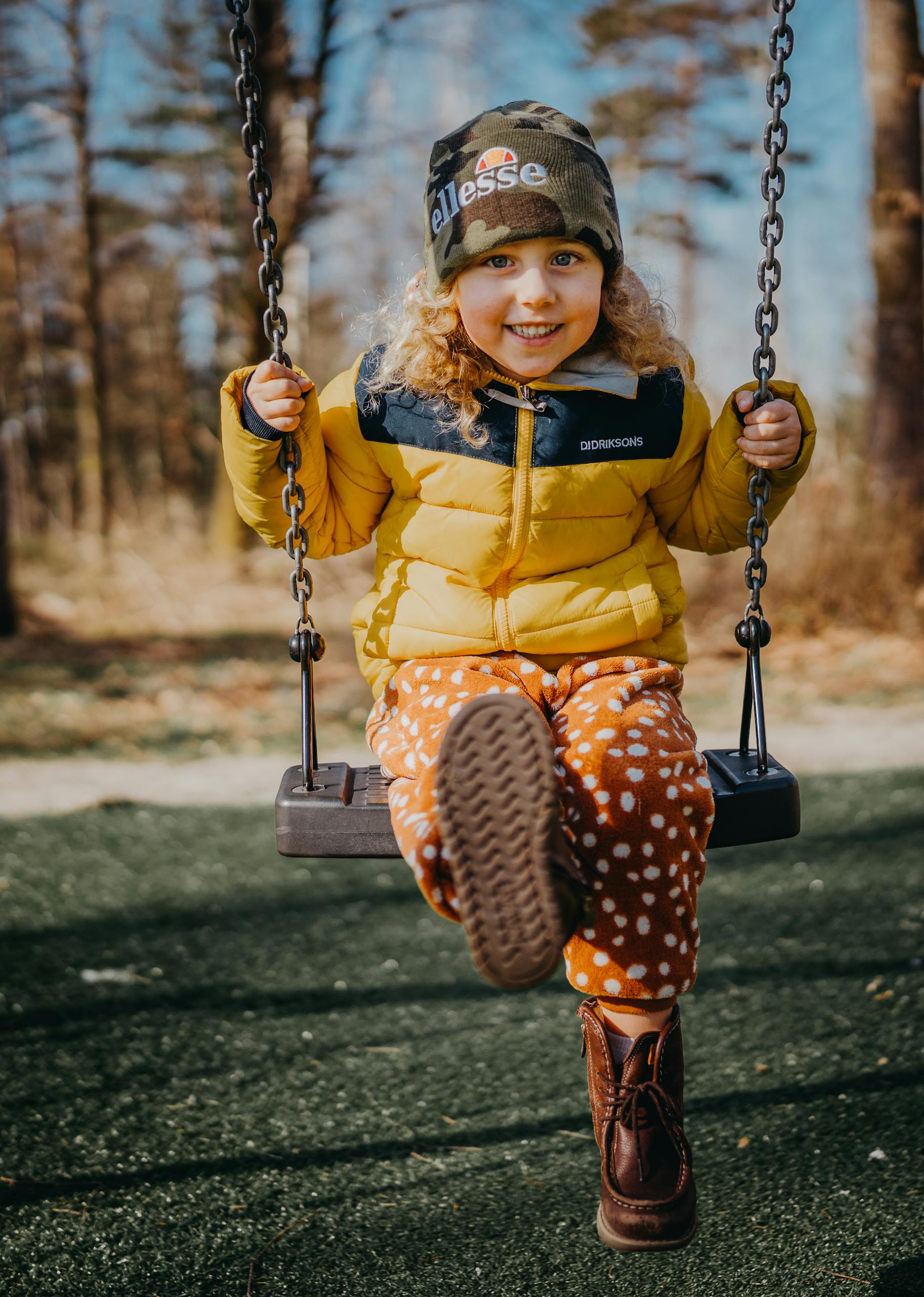 Smiling child in yellow jacket swinging outdoors. Bright autumn day with happiness and play.